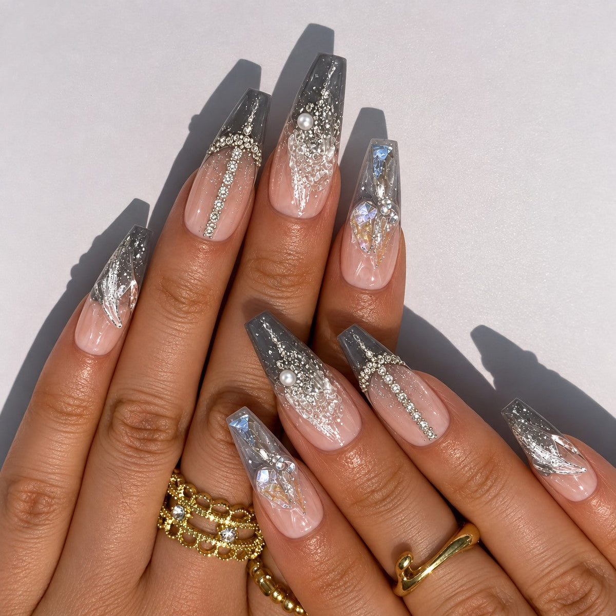 hand: Long coffin press-on nails in smoky grey and clear with crushed silver foil and raised crystal shards.
