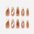 catalog: Long coffin nails in sheer nude with gold foil outlines, small white flowers, cream tips and tiny crystals.