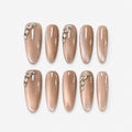 catalog: Long almond press-on nails in glossy mocha nude with pearly shimmer and small clear crystal accents near the cuticle.