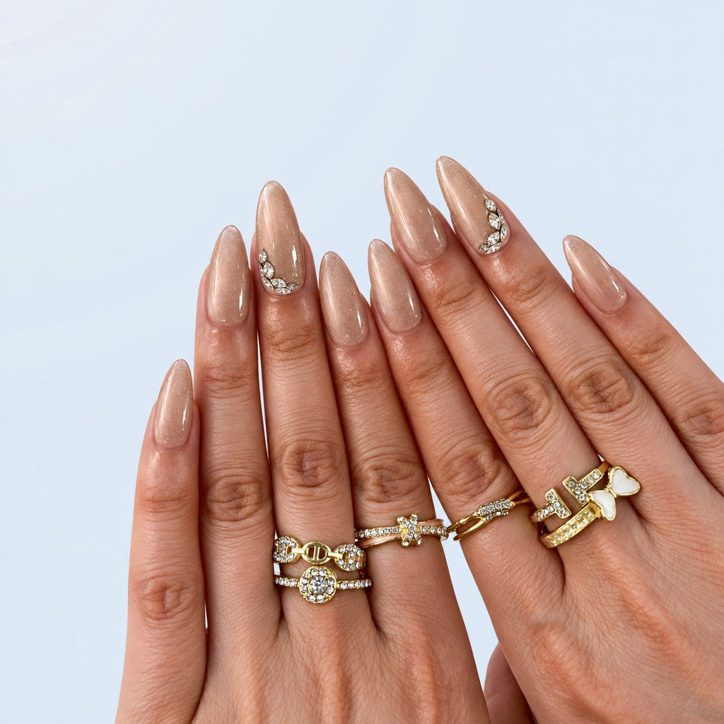 hand: Long almond press-on nails in glossy mocha nude with pearly shimmer and small clear crystal accents near the cuticle.