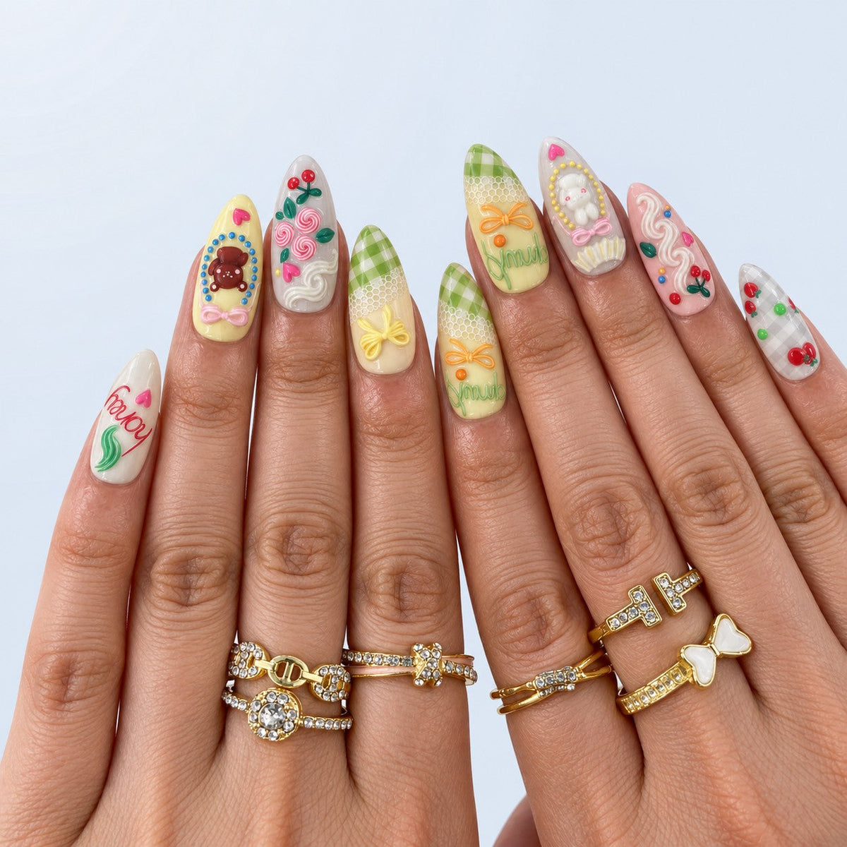 hand: Medium almond press-on nails in pastel pink, yellow and mint with 3D bunny, bear, bow, cherry and cream swirl charms.