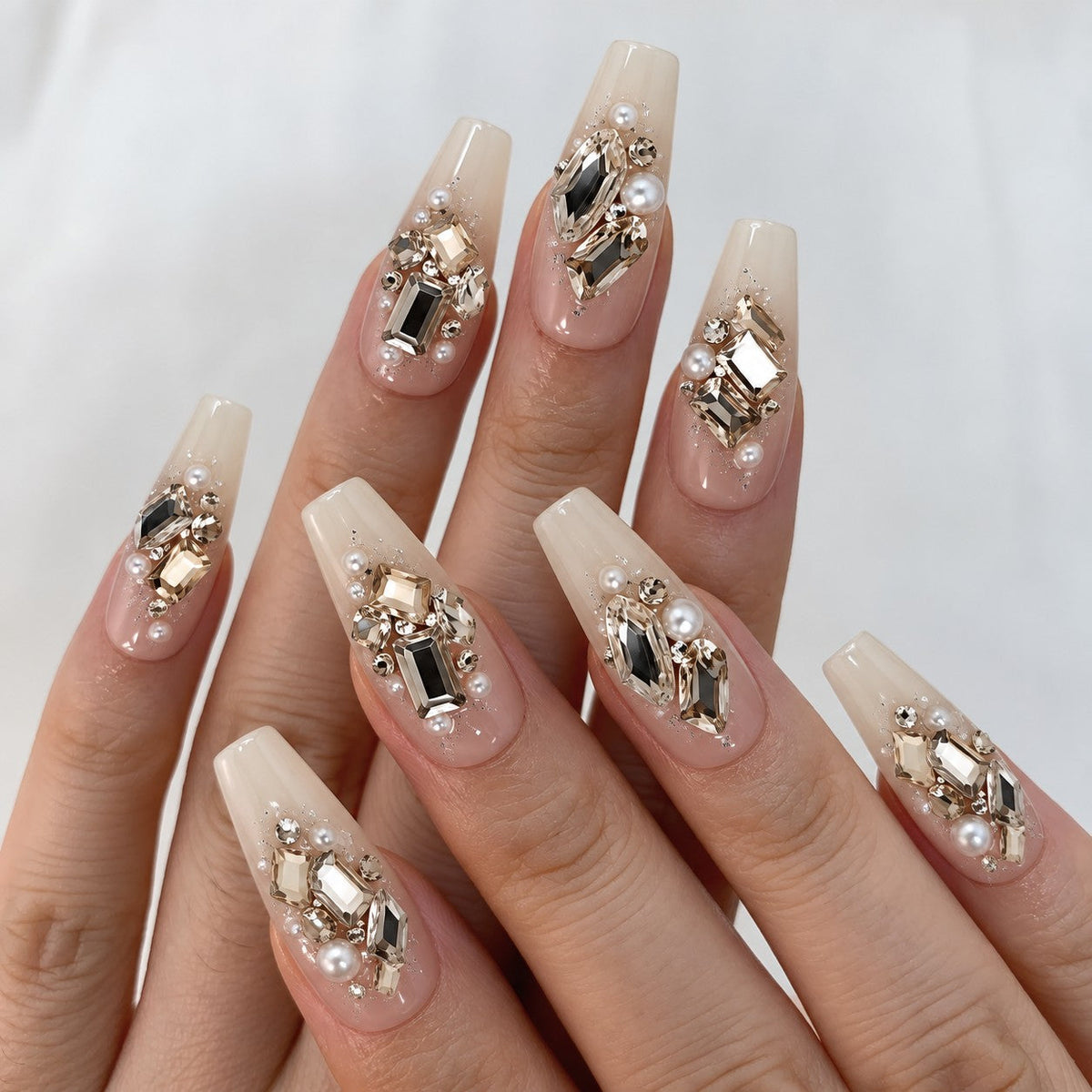 hand: Long coffin press-on nails in sheer ivory with clusters of champagne and clear crystals, pearls and fine glitter.