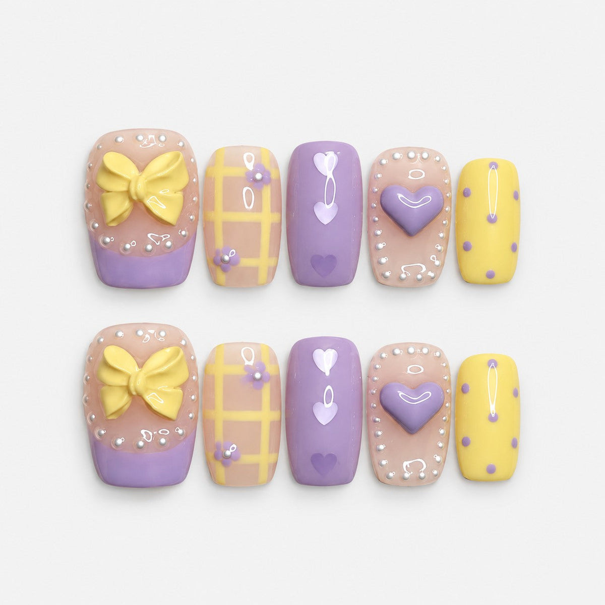 catalog: Short square press-on nails in lilac and pastel yellow with a sculpted bow, a raised heart, painted hearts, grid lines and white dot borders.