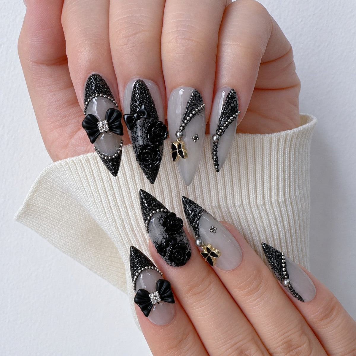hand: Long stiletto nails in frosted grey with black lace print, a pearl framed cameo, black bows and sculpted black roses.