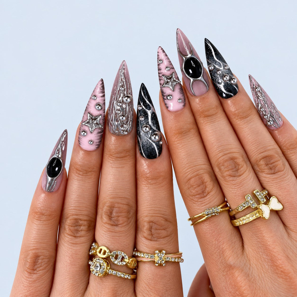 hand: Long stiletto press-on nails in mauve pink and black with liquid chrome silver detailing, black cabochon stones, silver beads and a sculpted star.