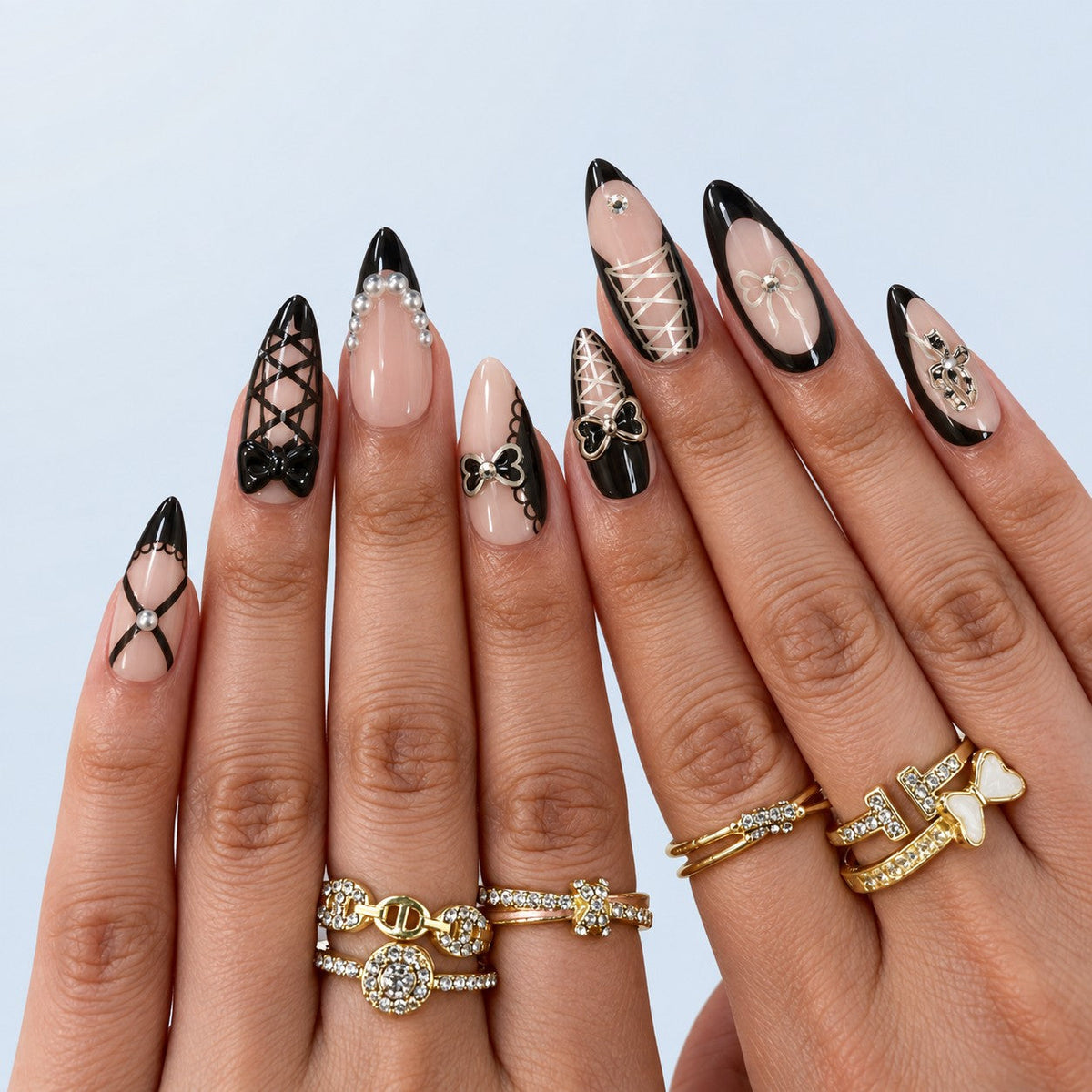 hand: Long almond nails with sheer nude bases, black French tips, painted black lace lines, grey pearls and raised glossy black bows.
