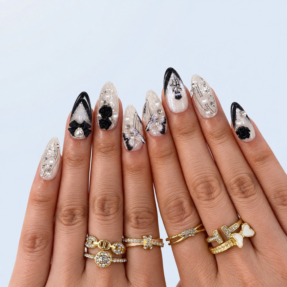 hand: Almond medium press-on nails in pearl white with glossy black tips, sculpted black roses, a black bow, pearls and rhinestones.