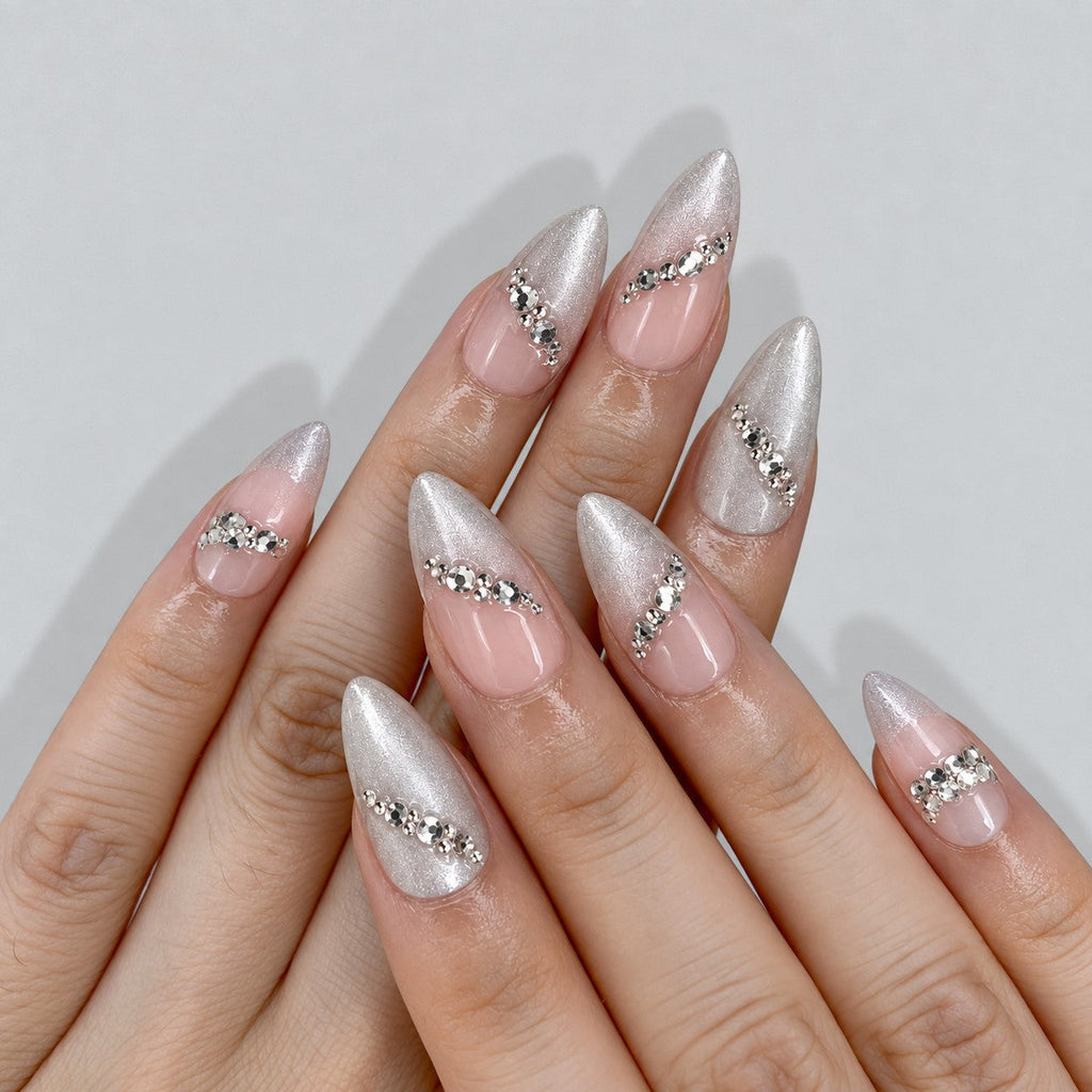 hand: Medium almond press-on nails in nude with pearly silver cat-eye shimmer, crystal accents along the edges and two large faceted stones.
