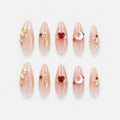 catalog: Long almond press-on nails in clear nude with gold leaf flecks, a red heart crystal with gold wings, and a pearl crescent moon charm.