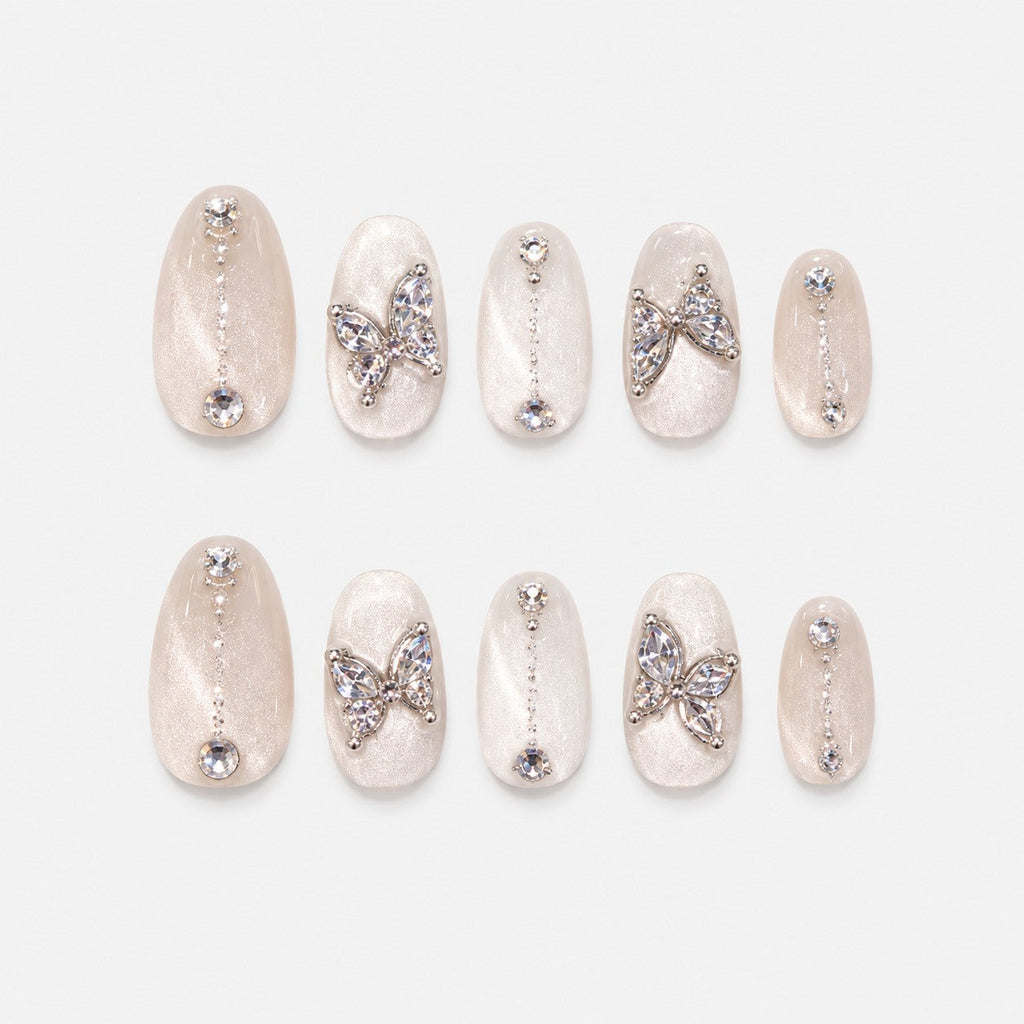 catalog: Almond medium press-on nails in pearly white cat-eye velvet with crystal butterfly charms and small rhinestone lines.