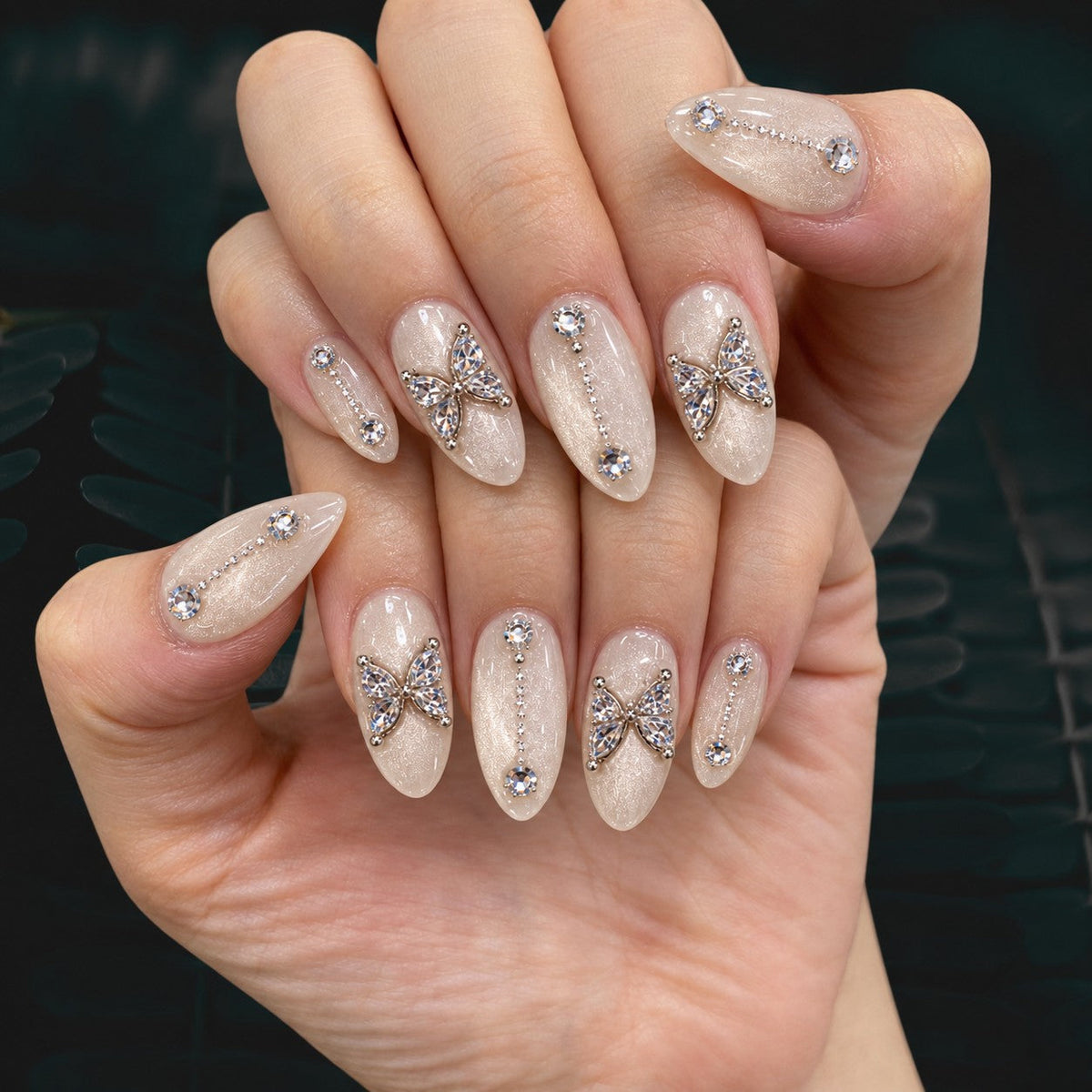 hand: Almond medium press-on nails in pearly white cat-eye velvet with crystal butterfly charms and small rhinestone lines.