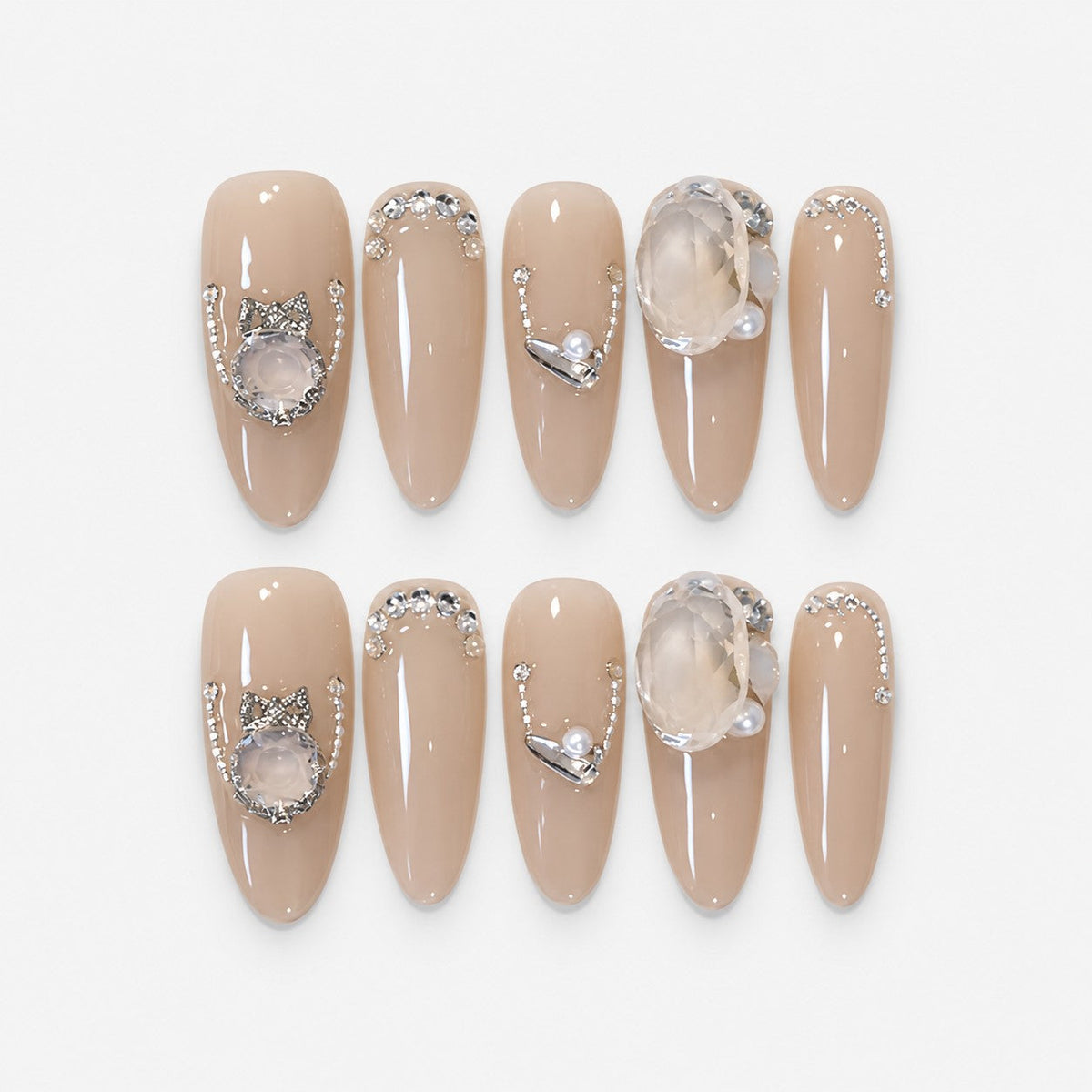catalog: Long almond press-on nails in glossy greige nude with silver rhinestone curves, a bow charm, a large clear crystal and small pearls.