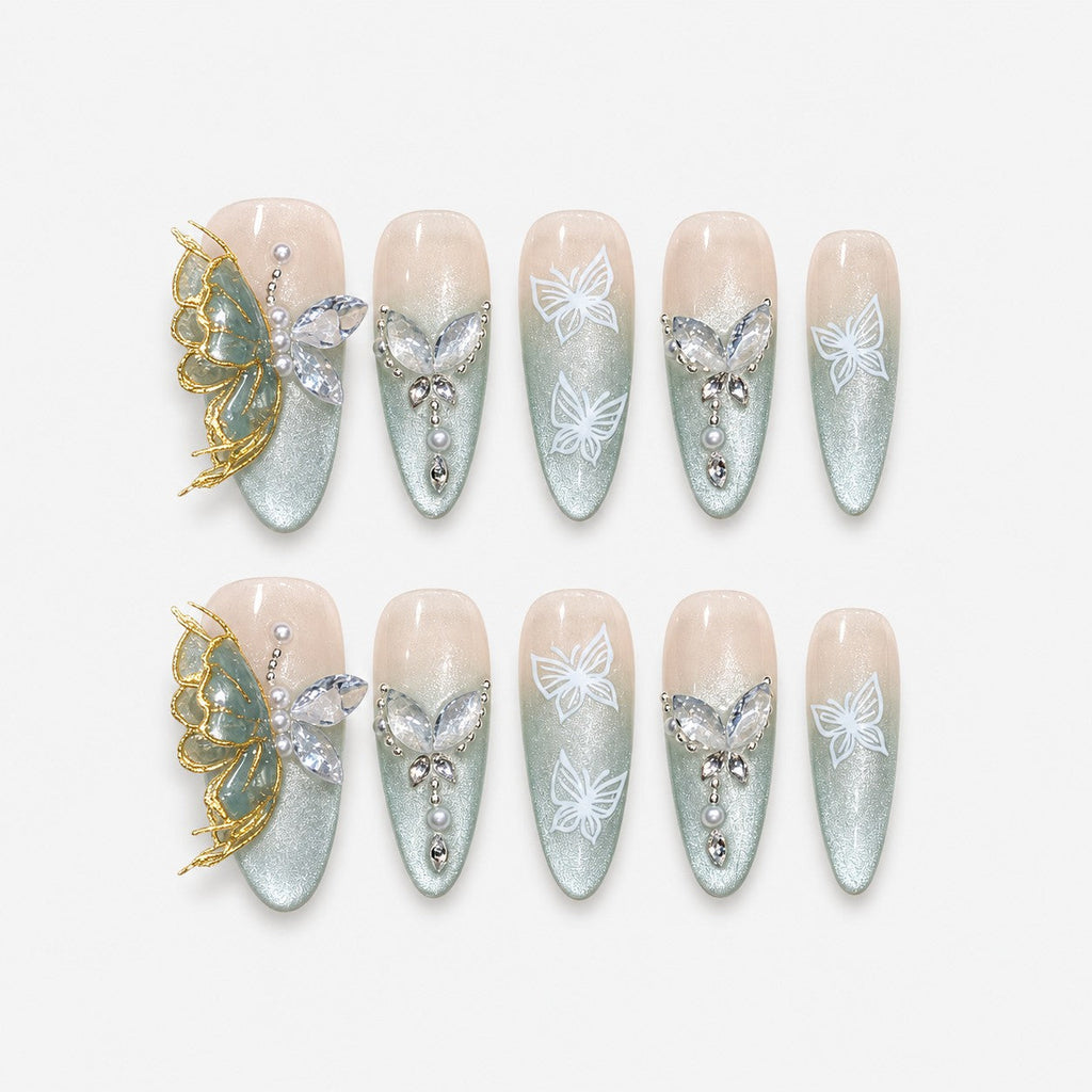 catalog: Long almond press-on nails with nude to sage green cat-eye gradient, white painted butterflies, crystals, pearls and a raised gold and stone butterfly charm.