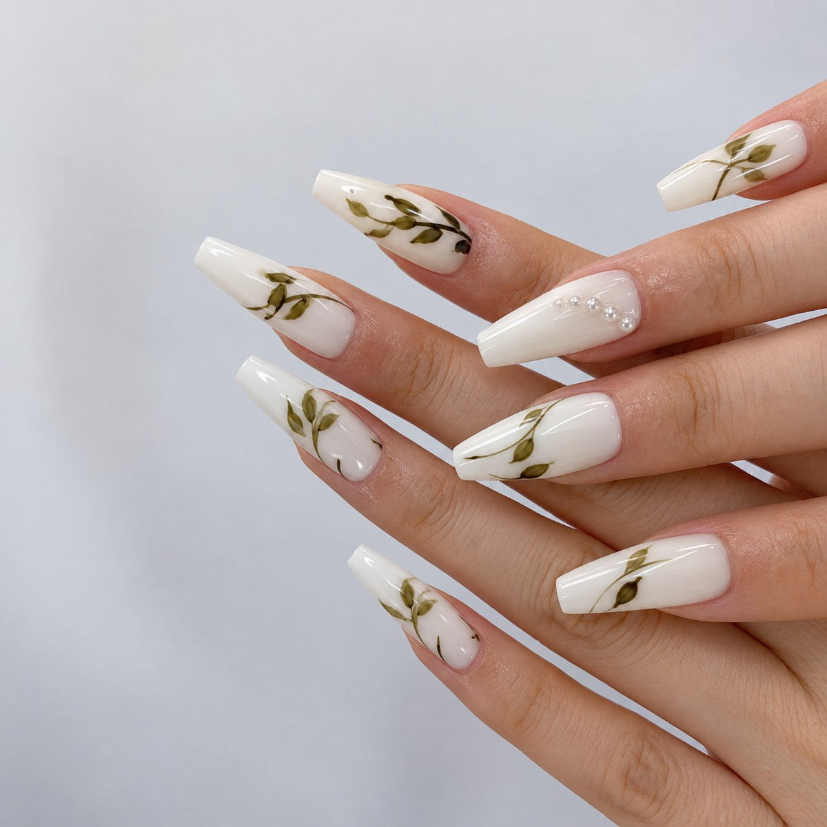 hand: Long coffin press-on nails in milky white with painted olive branches and small white pearls near the cuticle.