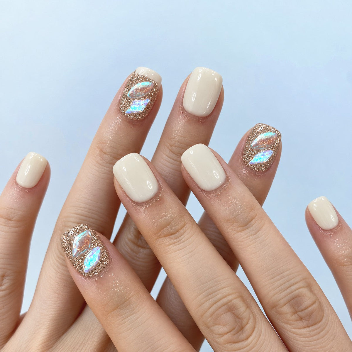 hand: Short square nails in creamy off white with two rose gold glitter accent nails holding iridescent aurora shards.