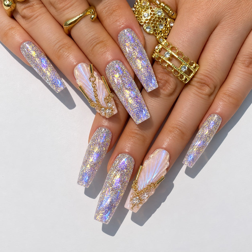 hand: Long coffin press-on nails with opal glitter, sculpted pearly shell wings, gold chains and gold crystal crowns.