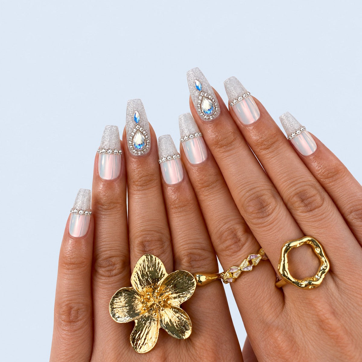 hand: Medium coffin nails in pink opal chrome with a rhinestone band, frosted silver glitter tips and teardrop crystal accents.