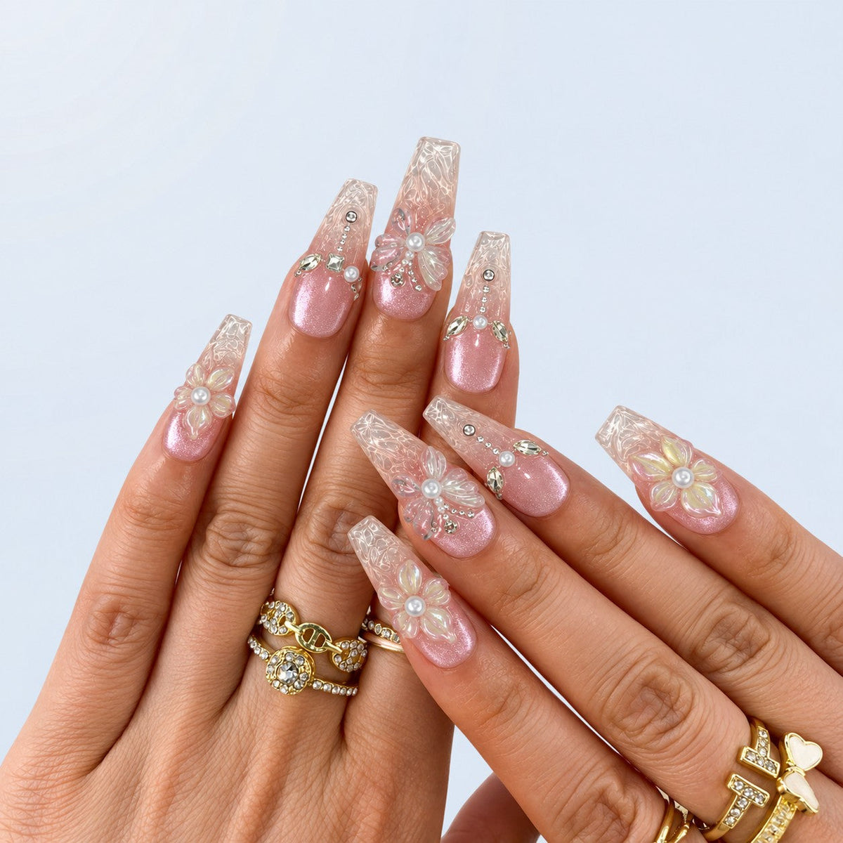 hand: Long coffin press-on nails in pearly pink cat-eye fading to clear tips, with raised white 3D flowers and butterflies, pearls and crystal chain details.