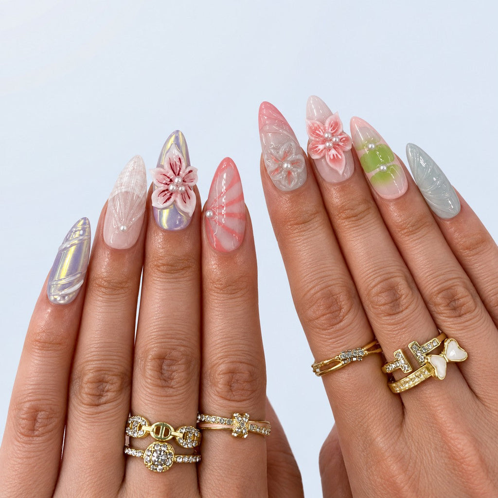 hand: Long almond press-on nails in milky pink, green and grey with sculpted 3D lilies and blossoms, red painted petal veins and small white pearls.