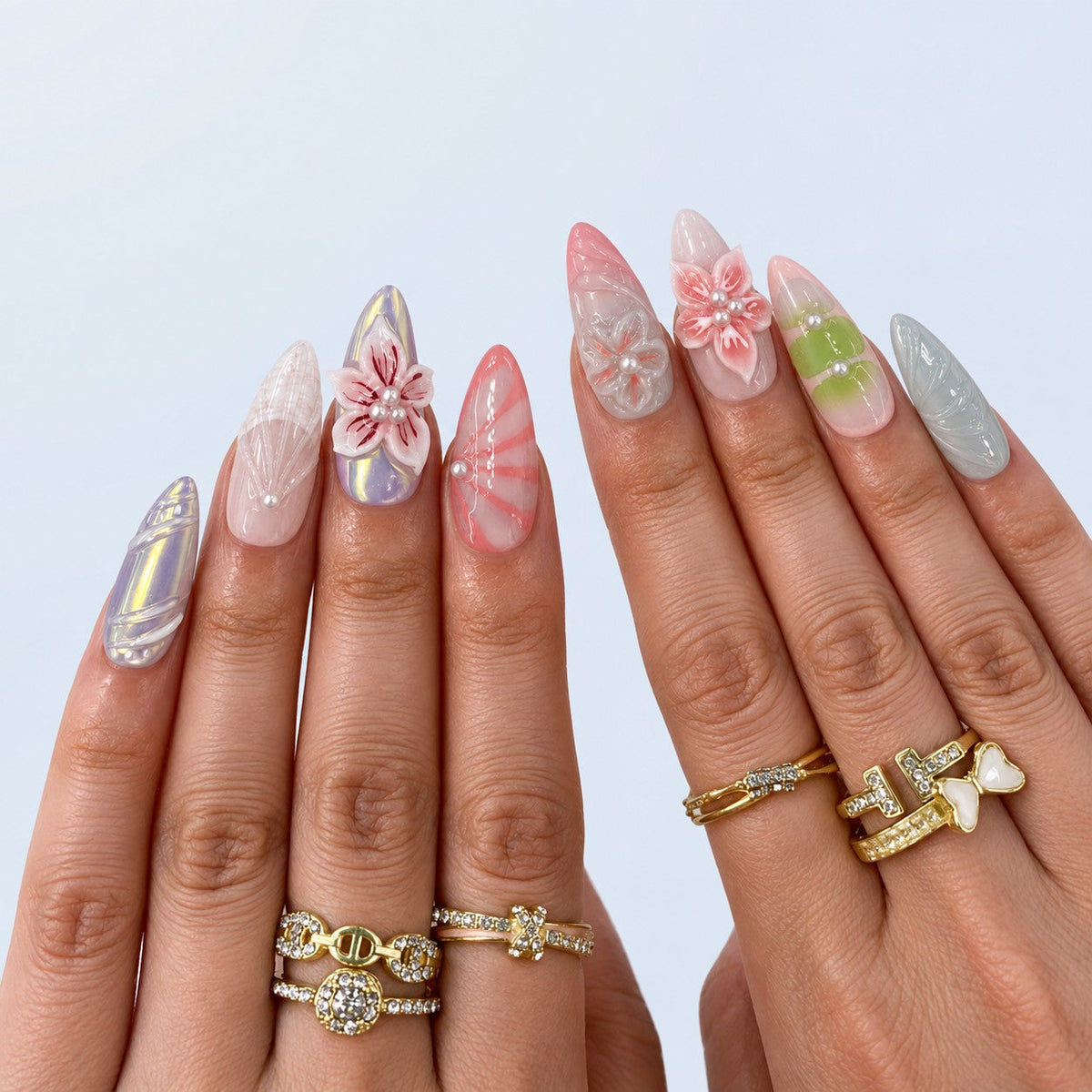 hand: Long almond press-on nails in milky pink, green and grey with sculpted 3D lilies and blossoms, red painted petal veins and small white pearls.