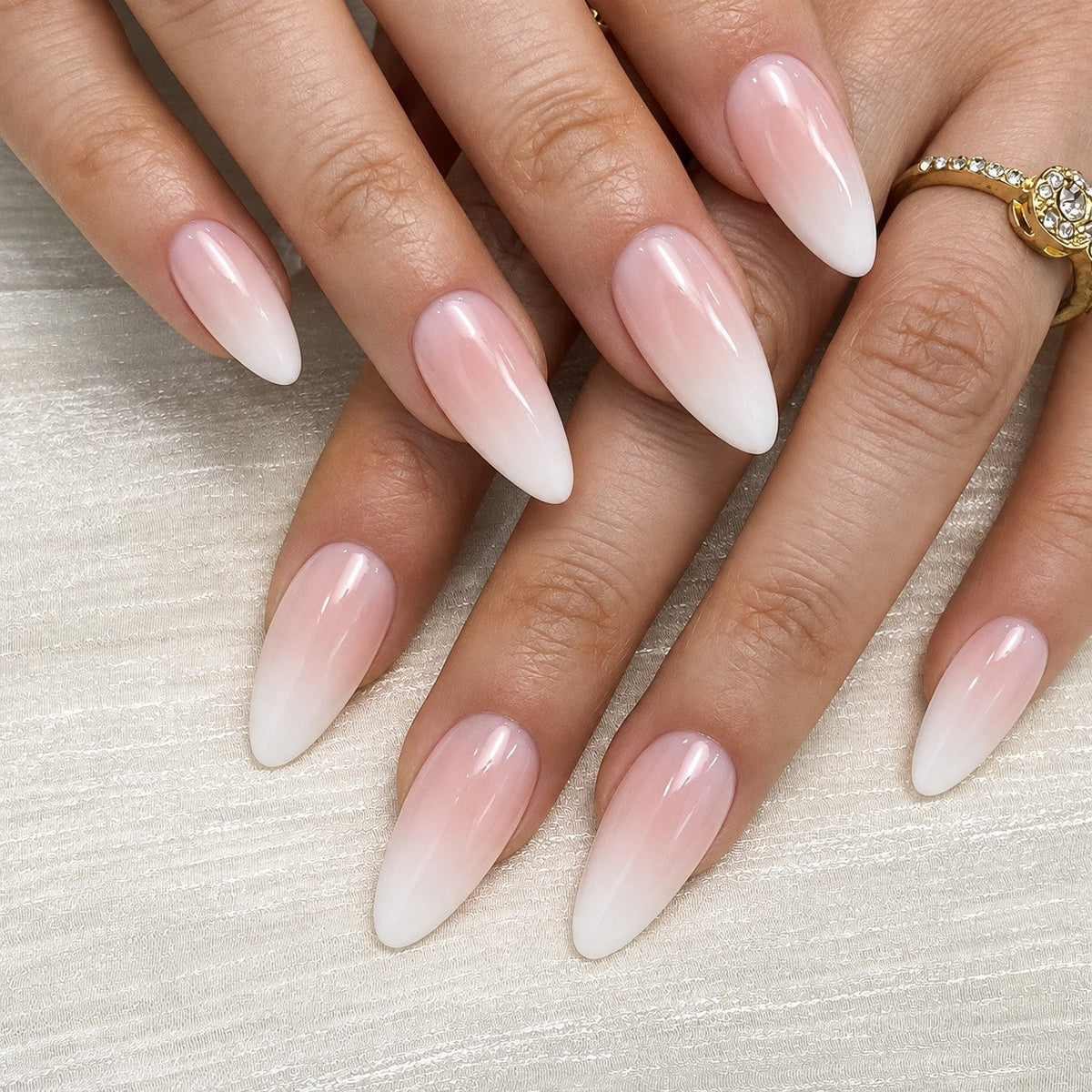 hand: Medium almond nails in a smooth nude to white ombre with a glossy finish and no added decoration.