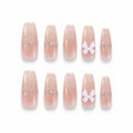 catalog: Long almond press-on nails in sheer pink with a row of small crystals along the cuticle line and a white 3D bow on the ring finger.