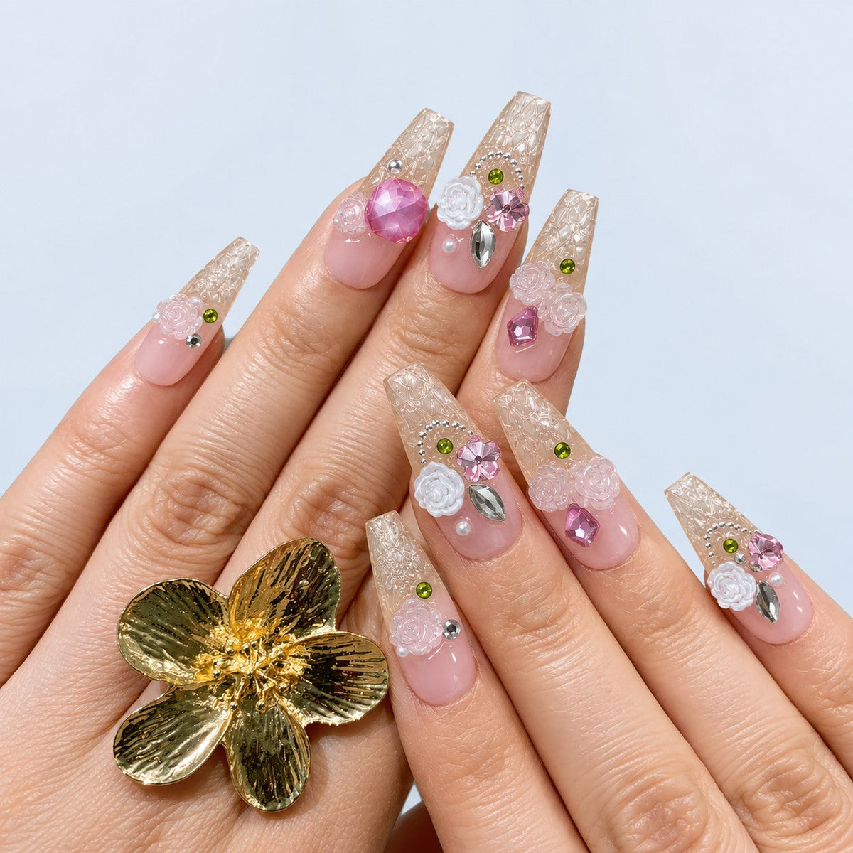 hand: Long pink and clear coffin nails with white sculpted roses, pink and lilac gems and small green beads.