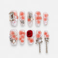 catalog: Long almond press-on nails with clear bases, sculpted coral rose flowers, pearls, clear and red crystals, and silver bow charms with chains.