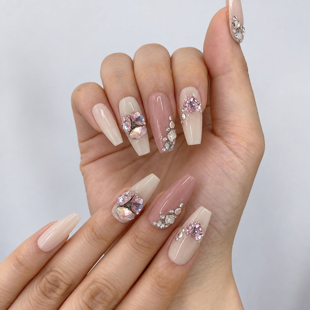 hand: Long coffin press-on nails in dusty pink and milky cream with clusters of clear crystals and large faceted pink oval and heart gemstones.