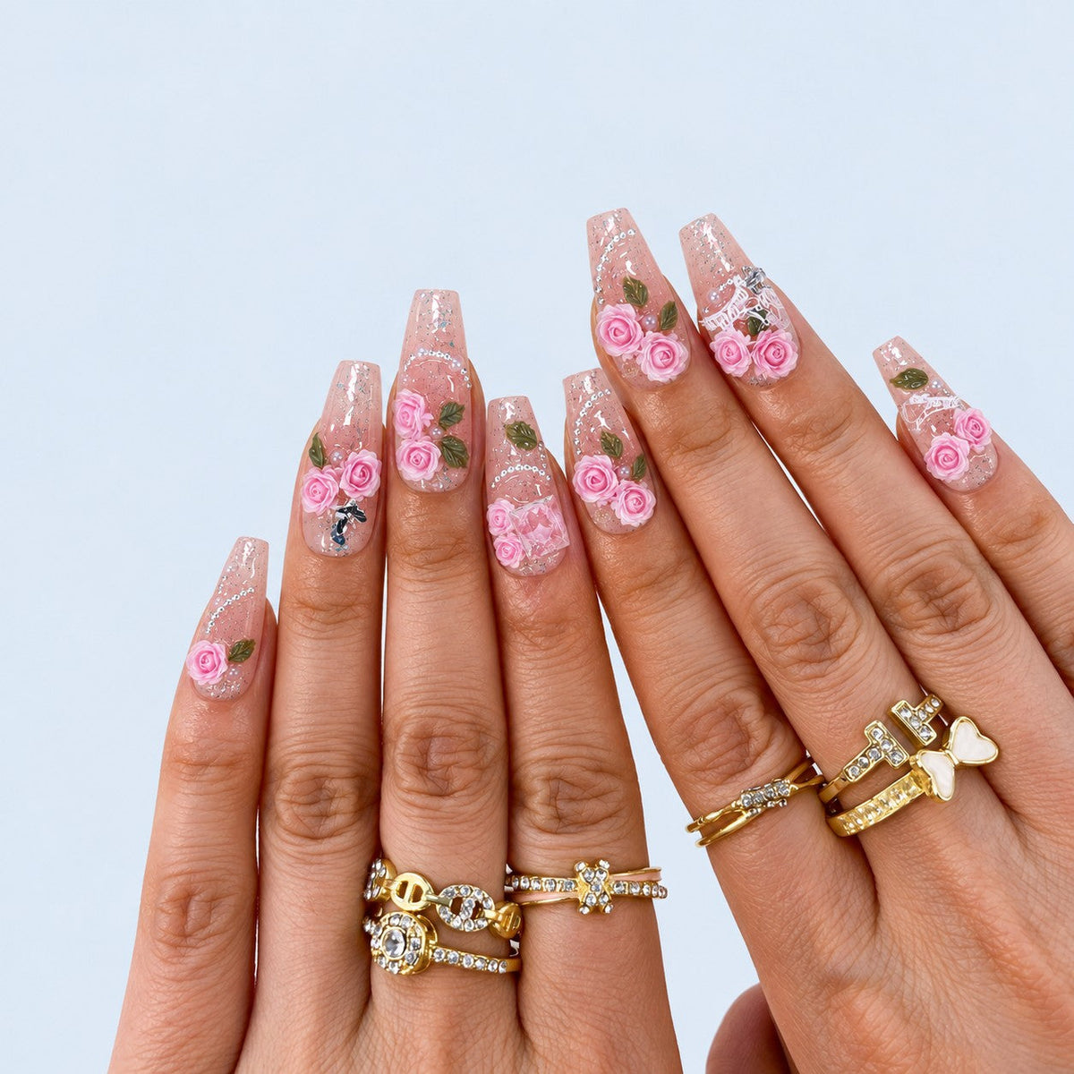 hand: Medium coffin press-on nails with a clear pink glitter base, sculpted pink roses with green leaves, pearls and a white lace bow.