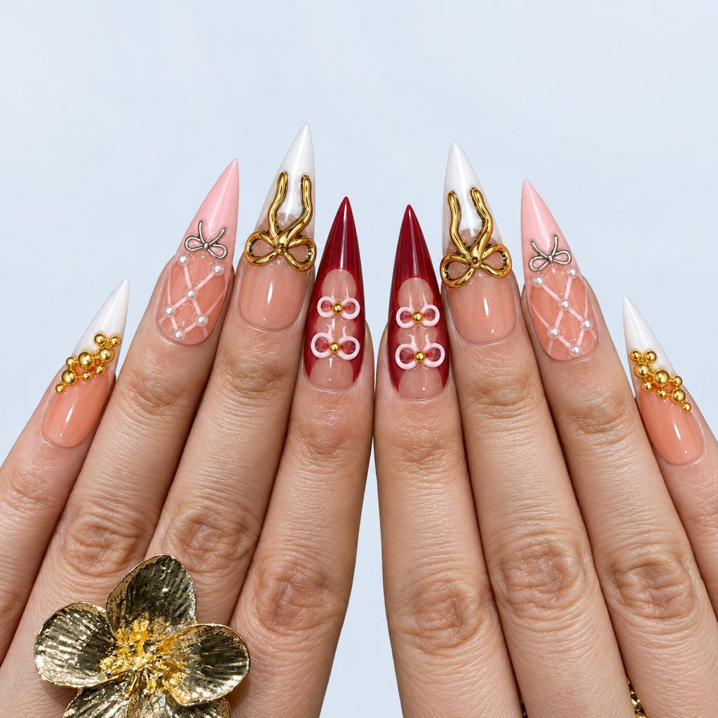 hand: Long stiletto press-on nails in peach and dark red with white tips, raised gold and silver bows, painted roses, gold beads and pearls.
