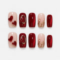 catalog: Medium almond press-on nails in deep red cat-eye with a sculpted rose in a gold ring, a gold-marbled nude nail and two glossy red hearts.