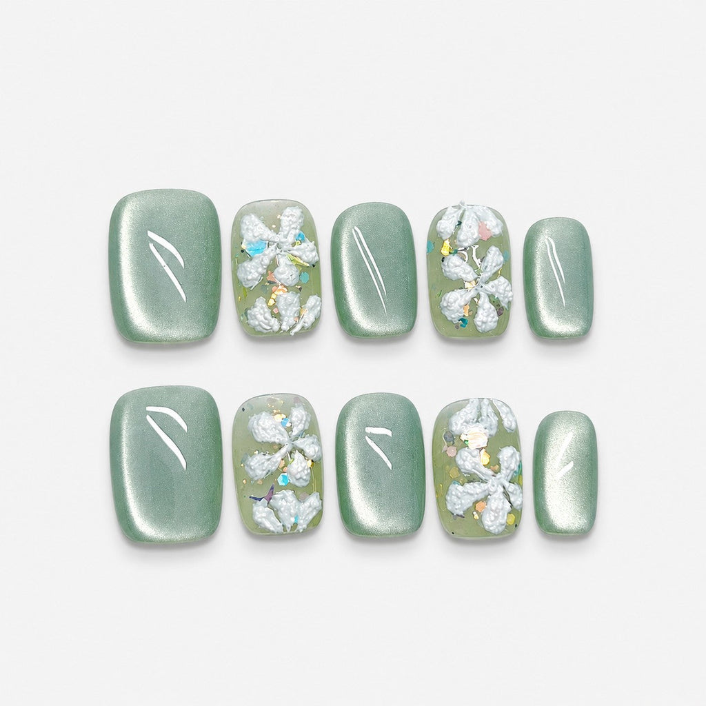catalog: Short square press-on nails in sage green cat-eye finish with raised white sculpted flowers and iridescent glitter flecks.