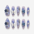 catalog: Long almond press-on nails in translucent blue and lilac marble with a white butterfly charm, a large blue gem, white curved lines and pearl details.