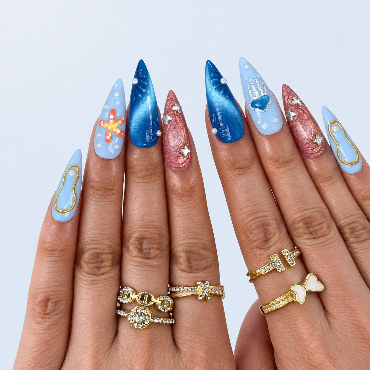 hand: Long stiletto nails in ocean blue, pale sky and shimmering rose with a painted starfish, silver jellyfish, sculpted shells, gold outlines and ivory pearls.