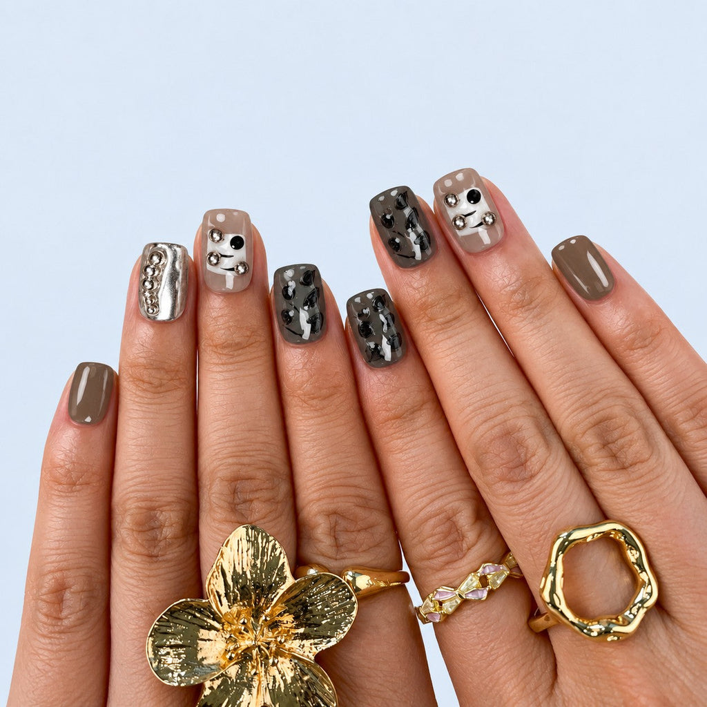 hand: Short square press-on nails in grey, taupe and black with silver chrome, pearls, metal beads and hand-painted line art, displayed in a wooden box.