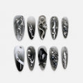 catalog: Long almond press-on nails in a smoky grey to black gradient with raised liquid chrome swirls, crystals, grey pearls and a rhinestone snake charm.