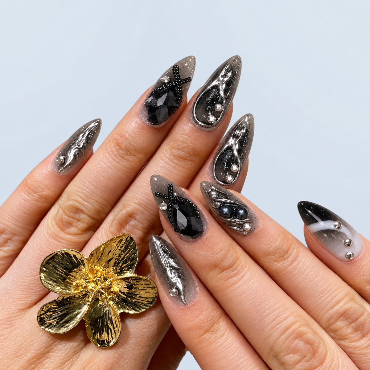 hand: Long almond press-on nails in a smoky grey to black gradient with raised liquid chrome swirls, crystals, grey pearls and a rhinestone snake charm.