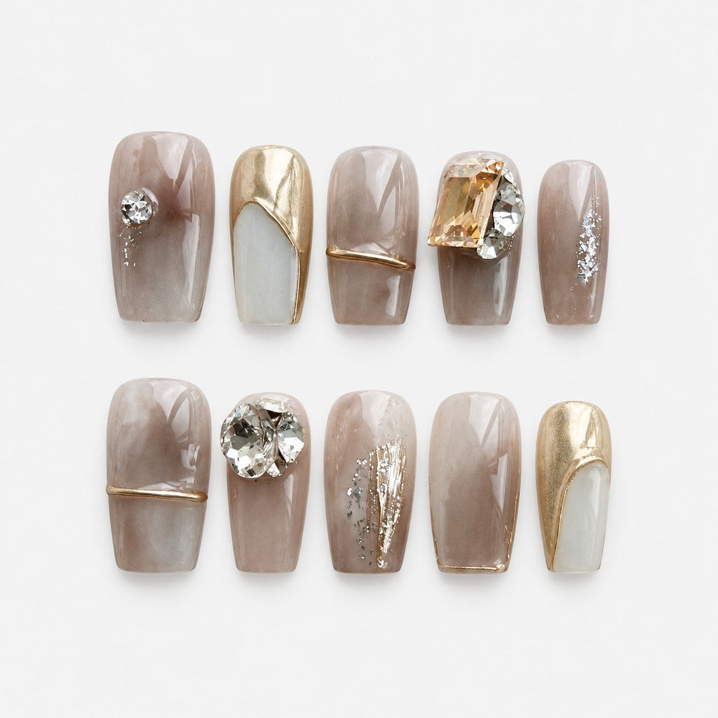 catalog: Medium square press-on nails in smoky taupe marble with gold outlines, a mirrored gold nail, silver foil detail and large clear and champagne crystals.