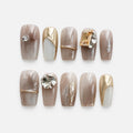 catalog: Medium square press-on nails in smoky taupe marble with gold outlines, a mirrored gold nail, silver foil detail and large clear and champagne crystals.
