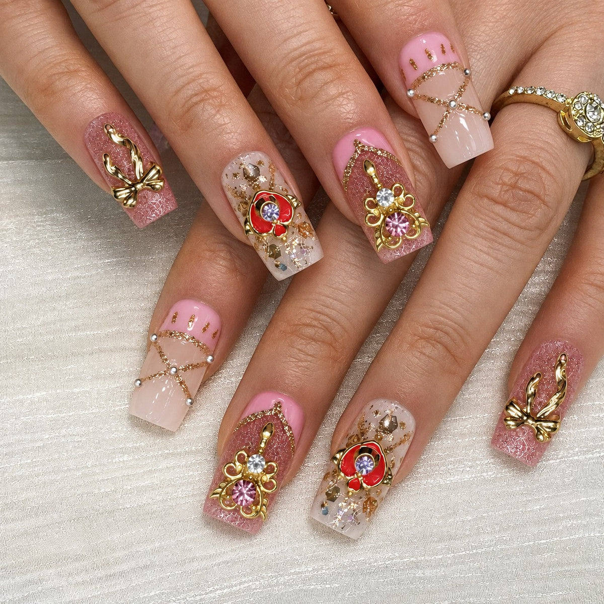 hand: Medium press-on nails in sheer pink with glittery fuchsia and teal hearts, gold crown and bow charms, crystals, gold flakes and pink stripes.