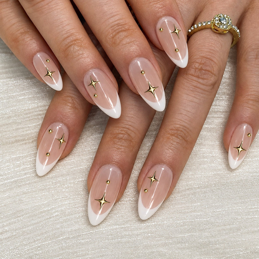 hand: Medium almond press-on nails with white French tips on a sheer pink base, gold star decals, thin gold lines and small gold studs.