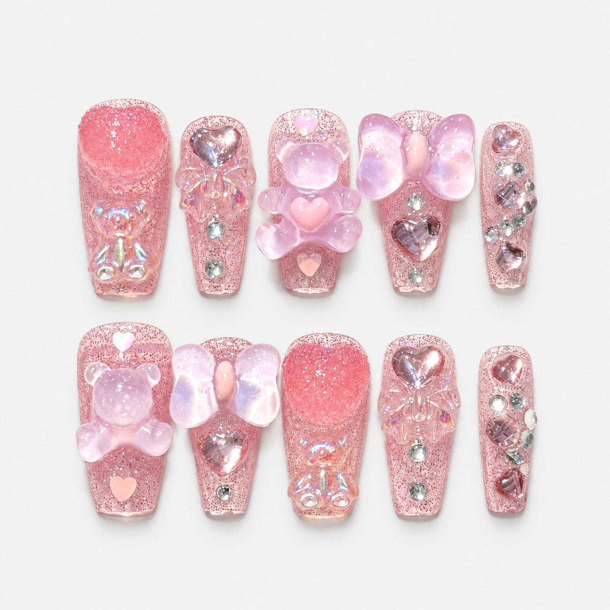 catalog: Long square press-on nails in sheer pink glitter with sculpted teddy bear charms, iridescent bows, glass hearts and small rhinestones.