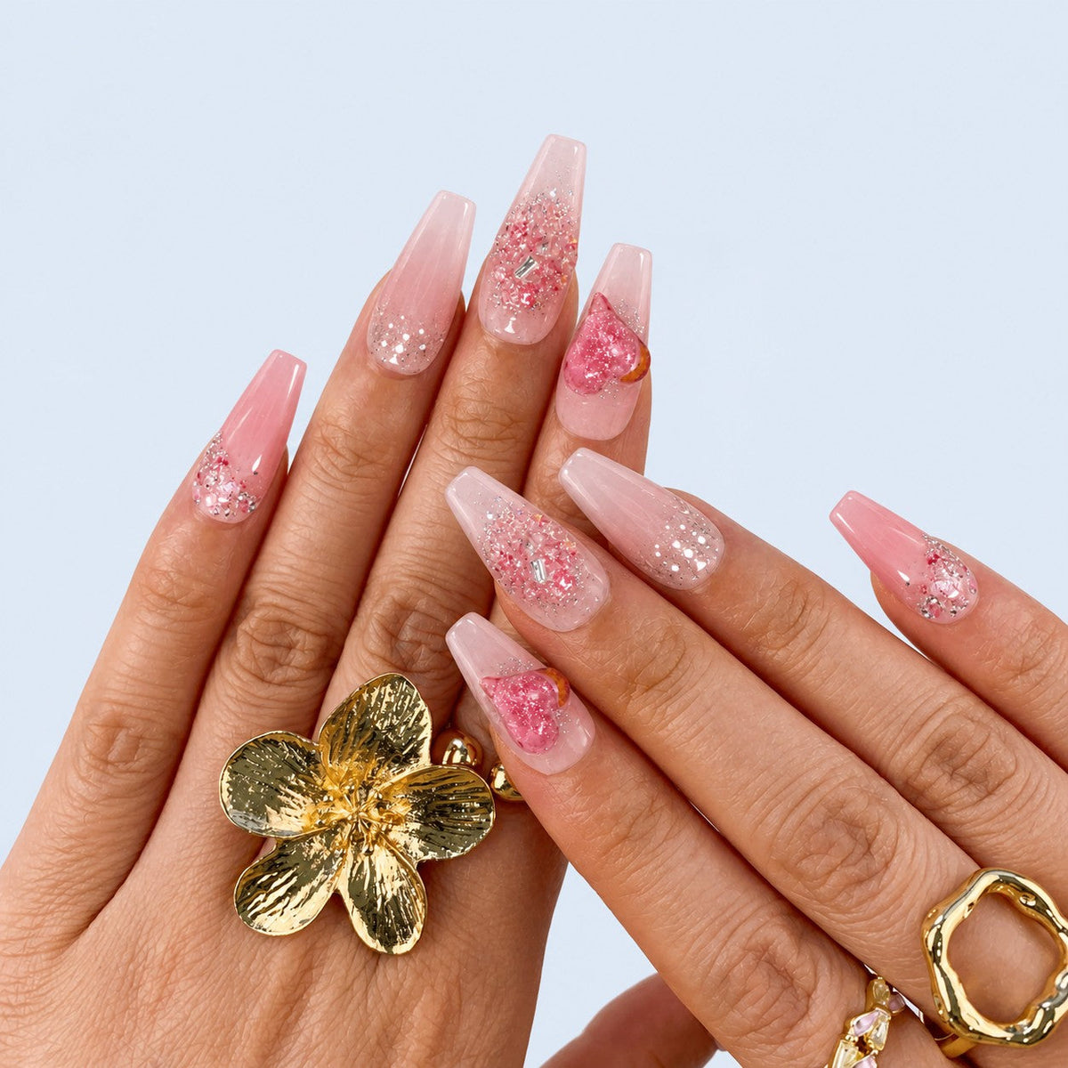 hand: Long coffin press-on nails in sheer pink with a raised glitter heart, silver beading and crystal grit at the cuticle.