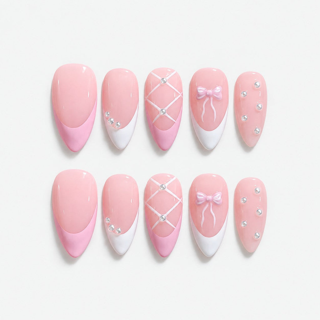 catalog: Medium almond press-on nails in pale baby pink with white French tips, a lattice nail, a pale bow and scattered clear crystals.