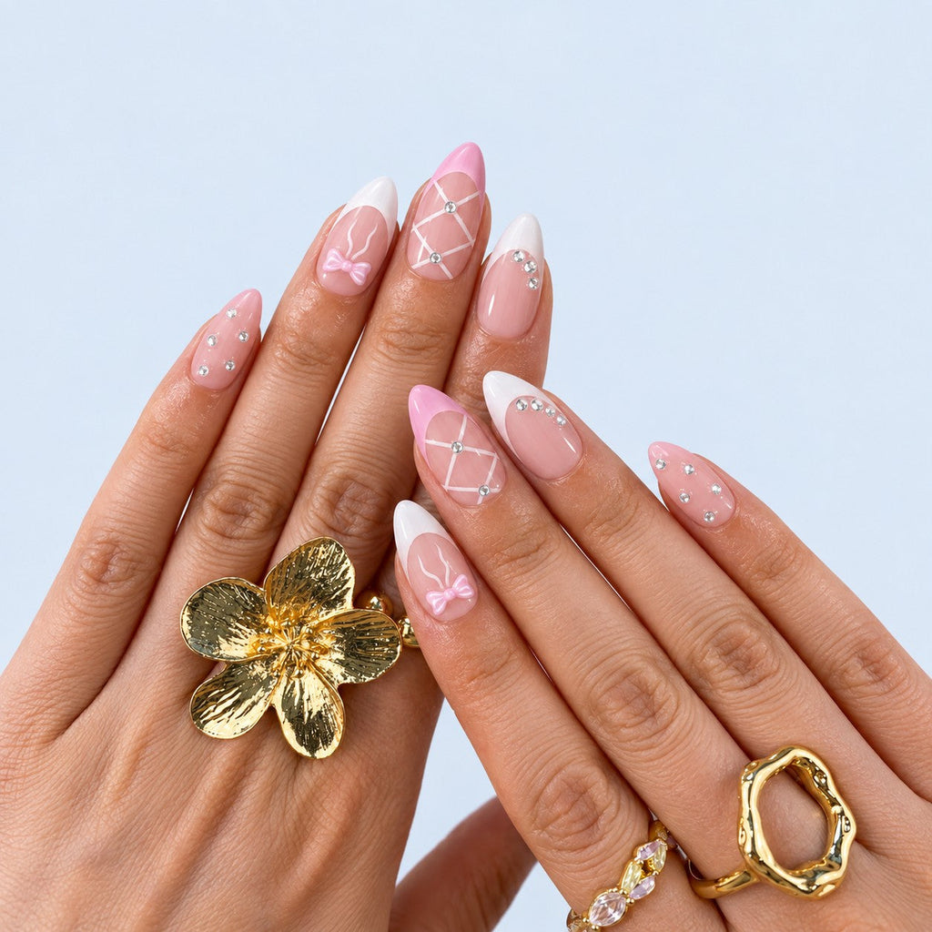 hand: Medium almond press-on nails in pale baby pink with white French tips, a lattice nail, a pale bow and scattered clear crystals.