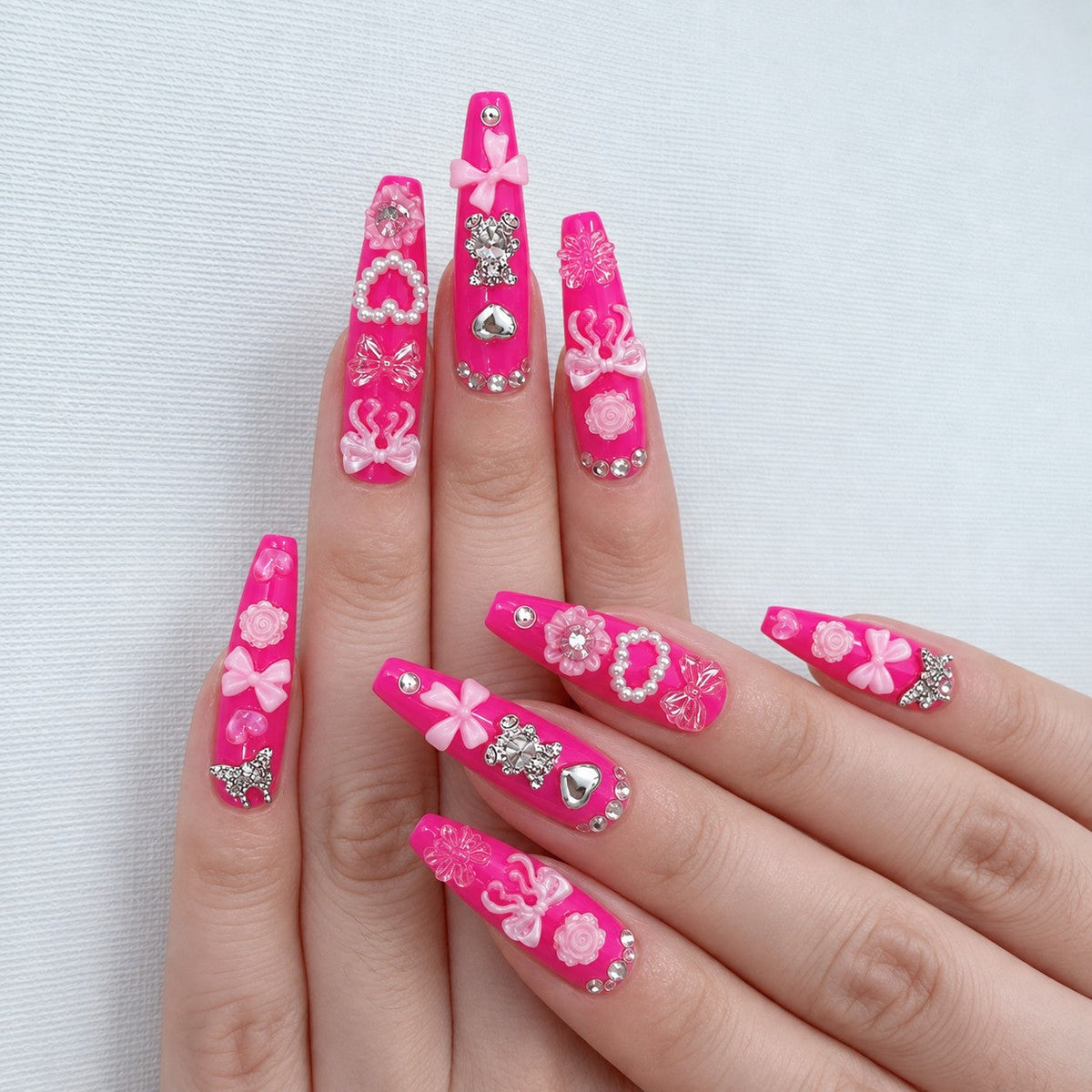 hand: Long coffin nails in glossy hot pink covered with silver hearts, pearl bows, roses and crystal charms.