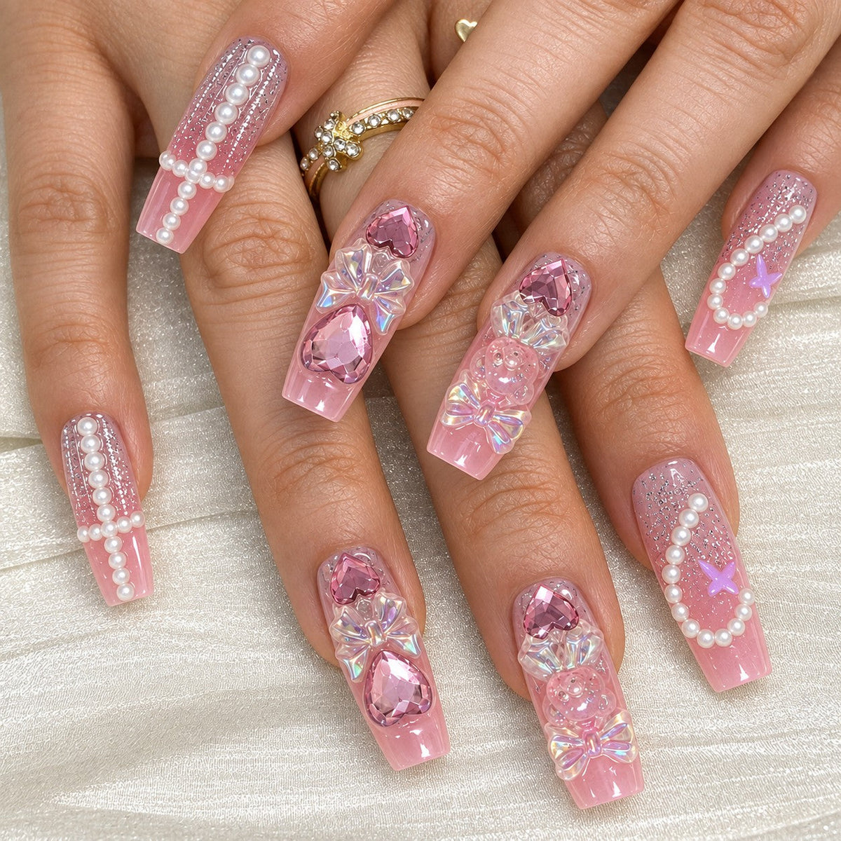 hand: Long pink coffin nails with iridescent 3D bows, bear charms, glassy hearts and curved pearl strands.