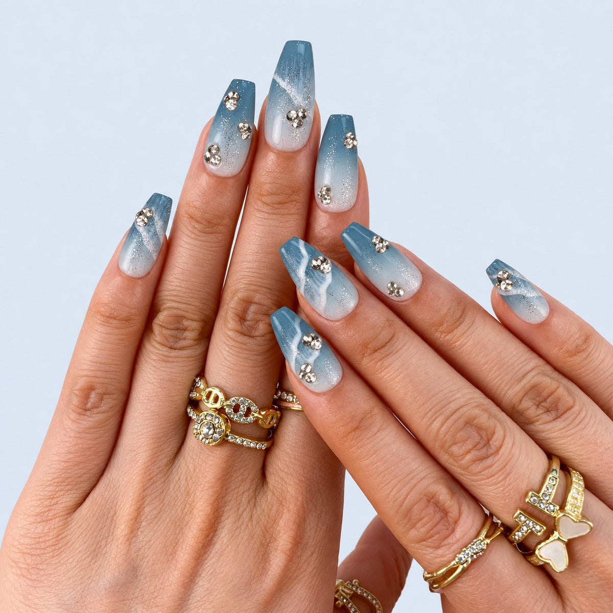 hand: Medium coffin press-on nails in blue to white gradient with silver glitter, sculpted white waves and clear rhinestone clusters.