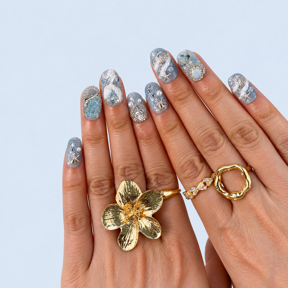 hand: Short oval press-on nails in pale blue shimmer with white sculpted coral, a jellyfish, silver shell and starfish charms, pearls and an aqua stone.